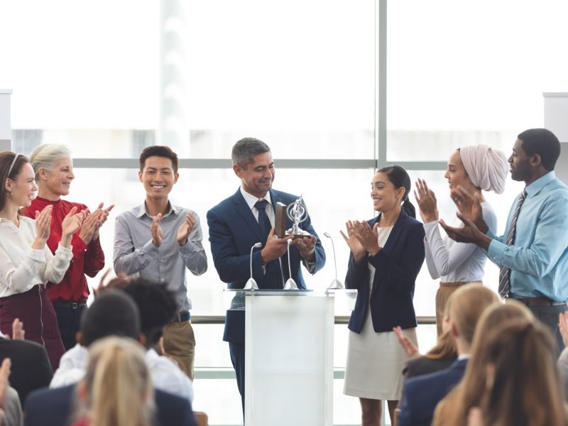 businessman-holding-award-on-podium-with-colleagues-at-business-seminar.jpg